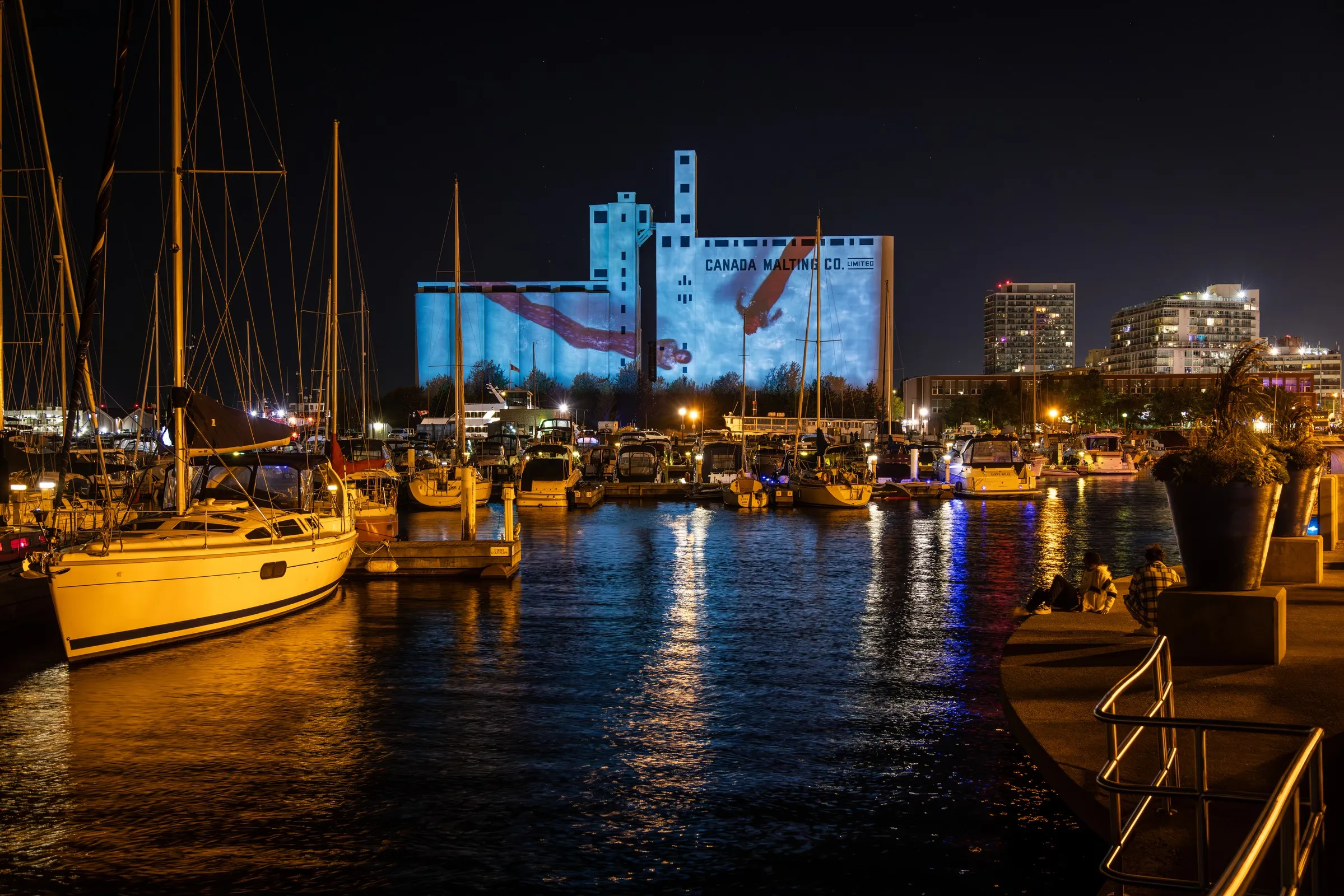 Riparia projection mapping on the Canada Malting Silos seen from across the street, full facade lit in blue aquatic light